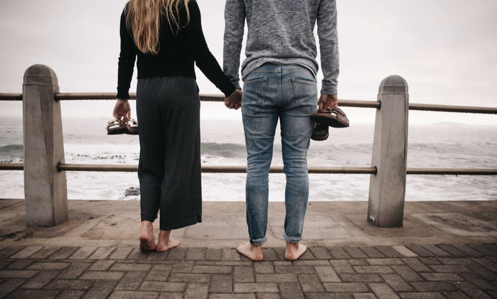 Junges Paar barfuß am Meer mit Birkenstock Schuhen in der Hand